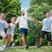 Group of joyful children playing outdoors with an instructor in a sunny park.