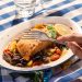 Delicious Mediterranean salmon with colorful vegetables on a blue checkered tablecloth.